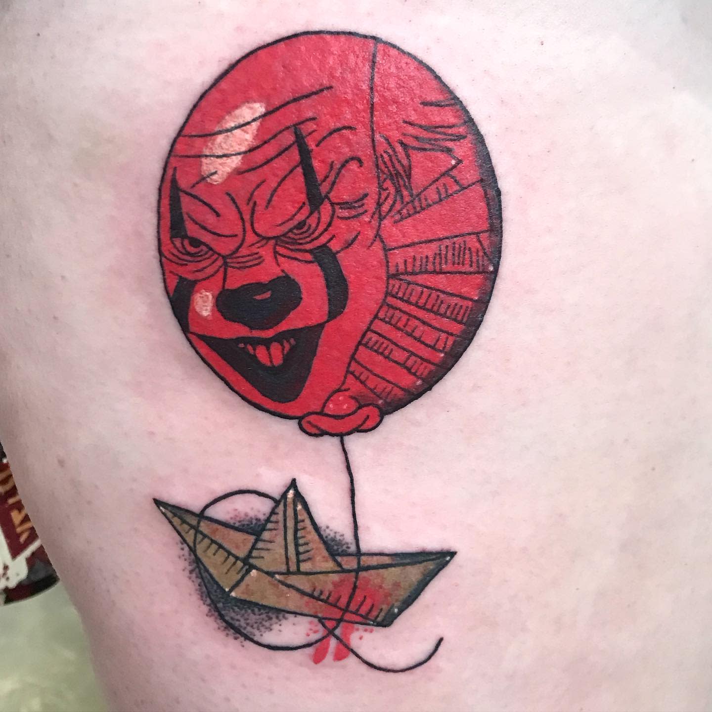 Minimalist Pennywise tattoo with a red balloon and paper boat, blending simplicity with horror